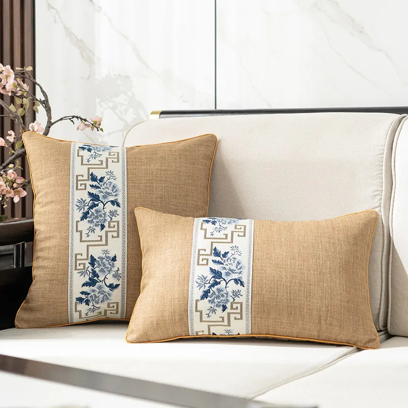 Deux coussins décoratifs en lin, ornés de motifs floraux bleus et de bordures géométriques, sont posés sur un canapé blanc dans un intérieur lumineux.