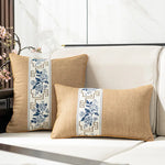 Deux coussins décoratifs en lin, ornés de motifs floraux bleus et de bordures géométriques, sont posés sur un canapé blanc dans un intérieur lumineux.