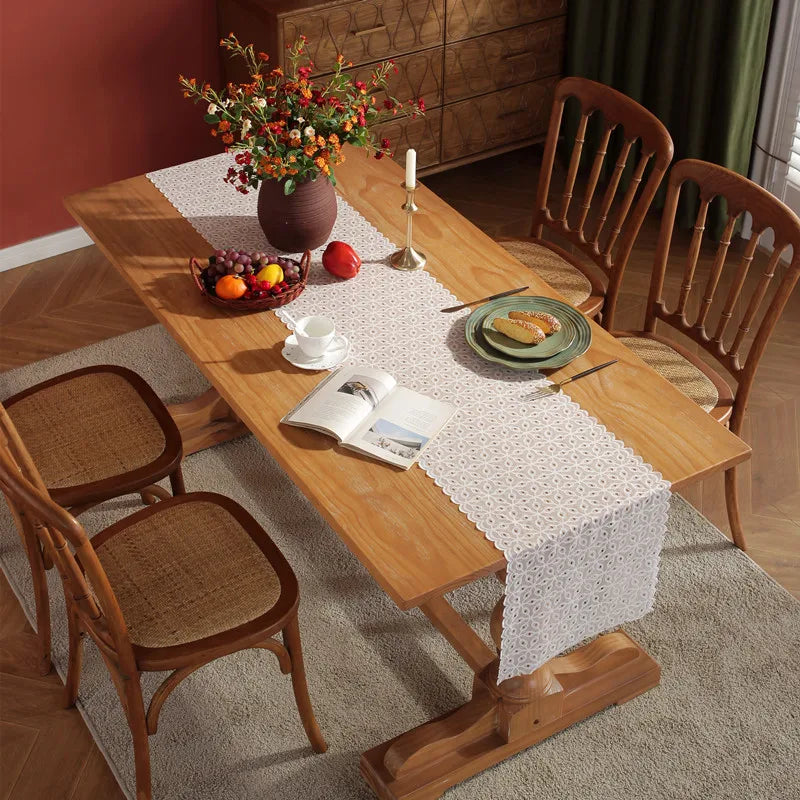 Une table en bois massif accueille une composition fleurie, un bol de fruits et une nappe blanche ouvragée, créant une ambiance chaleureuse et conviviale dans cette pièce.
