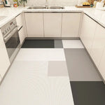 Un sol de cuisine moderne composé de dalles grises et blanches aux motifs graphiques, complétant harmonieusement les armoires beiges et le plan de travail en granite.