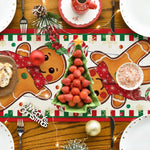 Une table festive de Noël décorée avec des biscuits en pain d'épice, une théière rouge, des fraises en forme d'arbre de Noël et d'autres éléments saisonniers.