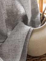 Voilage occultant gris clair en tissu texturé drapé sur un vase en céramique.