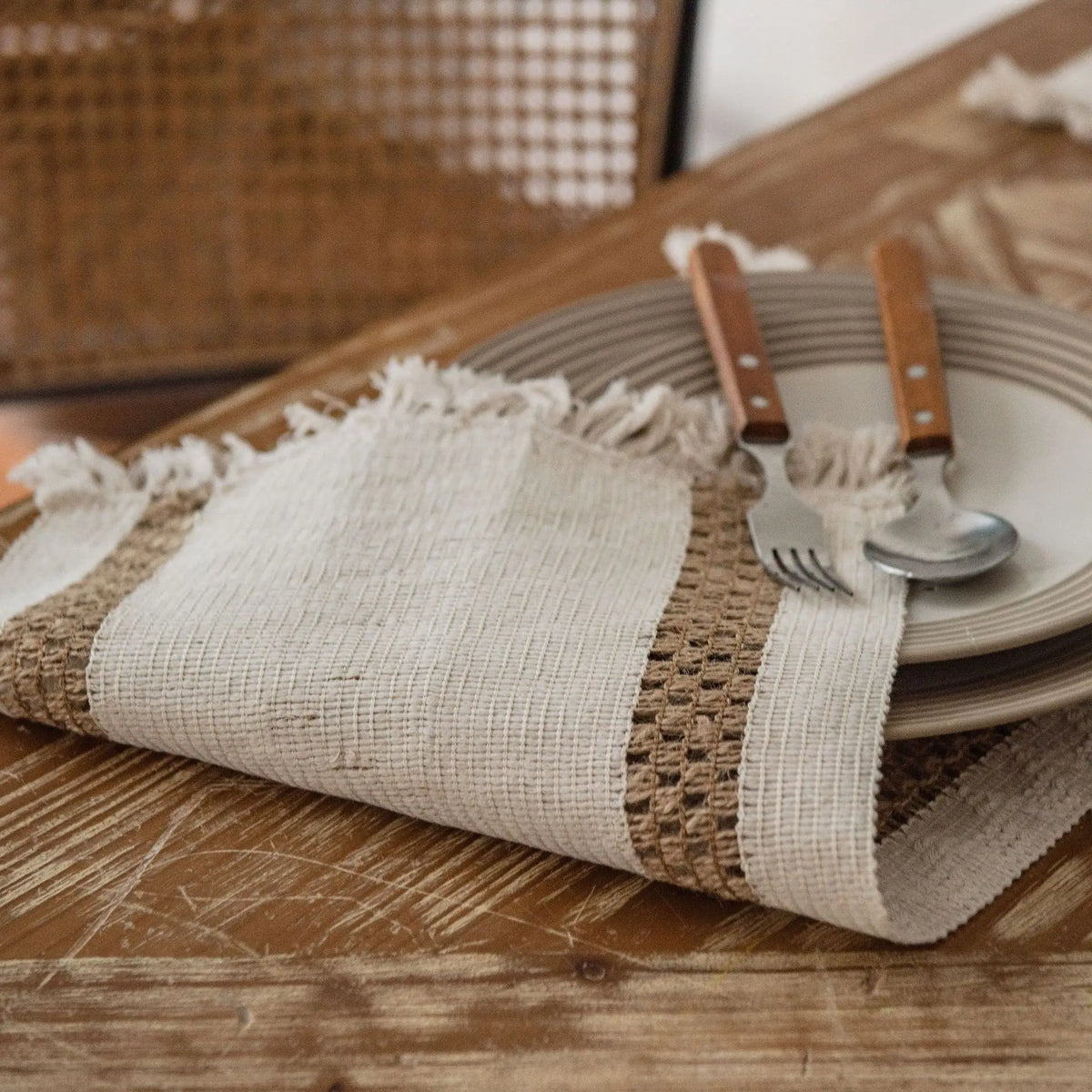 Une nappe en lin naturelle avec une bordure texturée, sur une table en bois rustique, entourée d'ustensiles de cuisine.