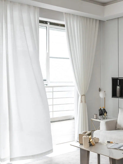 Voilage blanc léger pour salon flottant devant une grande fenêtre.