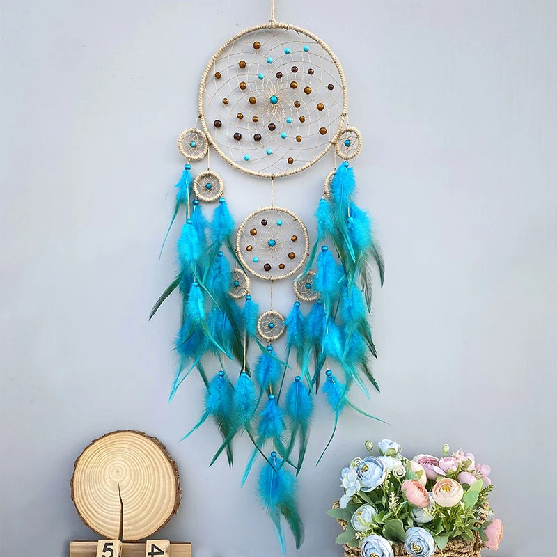 Magnifique attrape-rêves artisanal aux nuances de bleu et de turquoise, orné de perles dorées et de plumes gracieuses, créant une atmosphère apaisante et mystique.