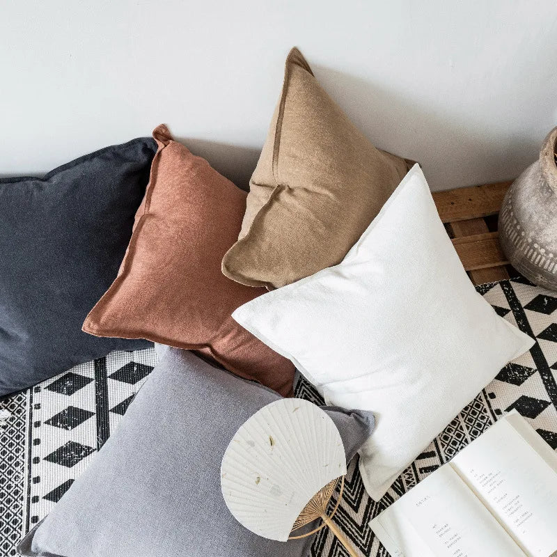 Cette image dépeint un arrangement de coussins décoratifs dans des tons de blanc, beige et noir, posés sur un tapis motif géométrique. L'ensemble crée une atmosphère chaleureuse et confortable dans un intérieur.