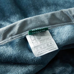 L'image montre une étiquette apposée sur un vêtement en tissu gris, indiquant les informations techniques et de lavage du produit.