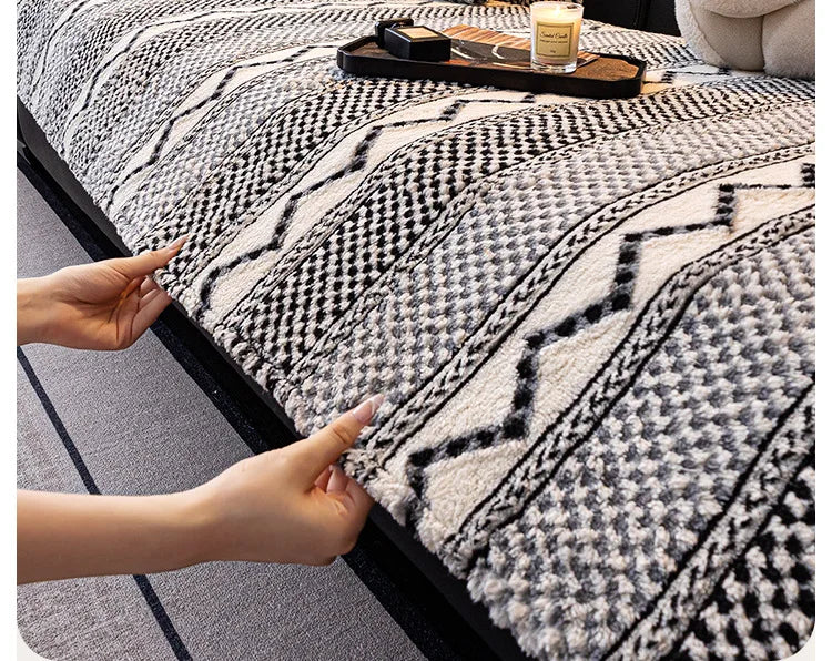 Une couverture en tricot gris et blanc, ornée de motifs géométriques, repose sur un lit, avec des accessoires de chambre posés dessus.