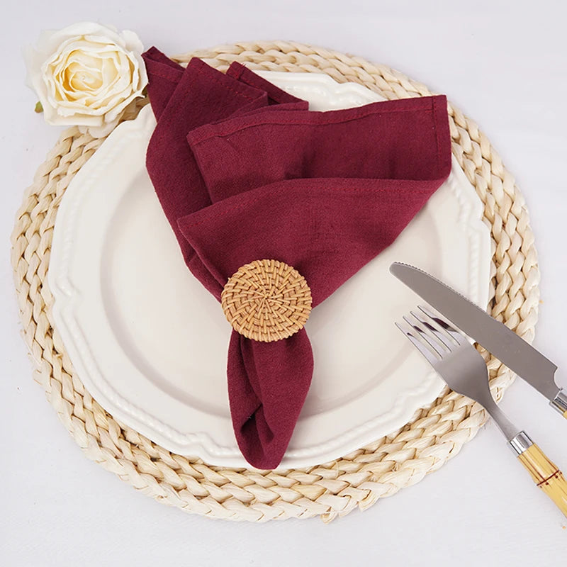 Une configuration élégante de table avec une assiette blanche, une serviette bordeaux élégamment nouée, une rose blanche et des ustensiles en métal.