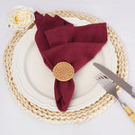 Une configuration élégante de table avec une assiette blanche, une serviette bordeaux élégamment nouée, une rose blanche et des ustensiles en métal.