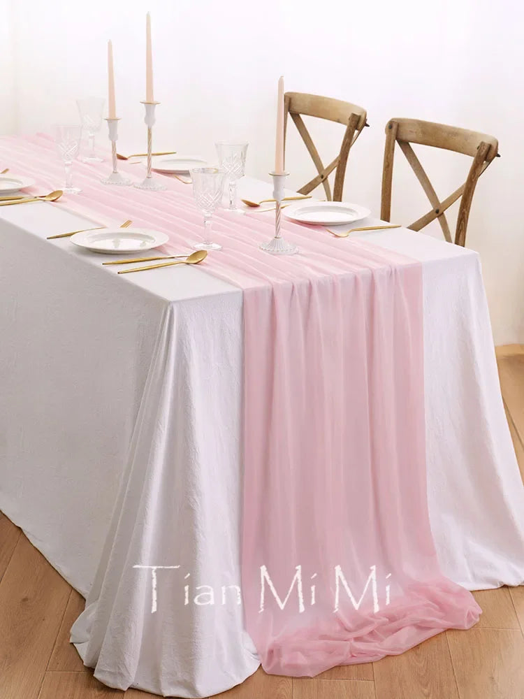 Une jolie table dressée avec élégance, comprenant une nappe blanche et rose, des verres et des couverts dorés, ainsi que des bougies pour créer une ambiance chaleureuse.
