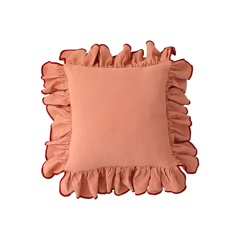 Coussin décoratif carré rose avec volants ornementaux sur les bords, créant un look élégant et romantique dans un intérieur.
