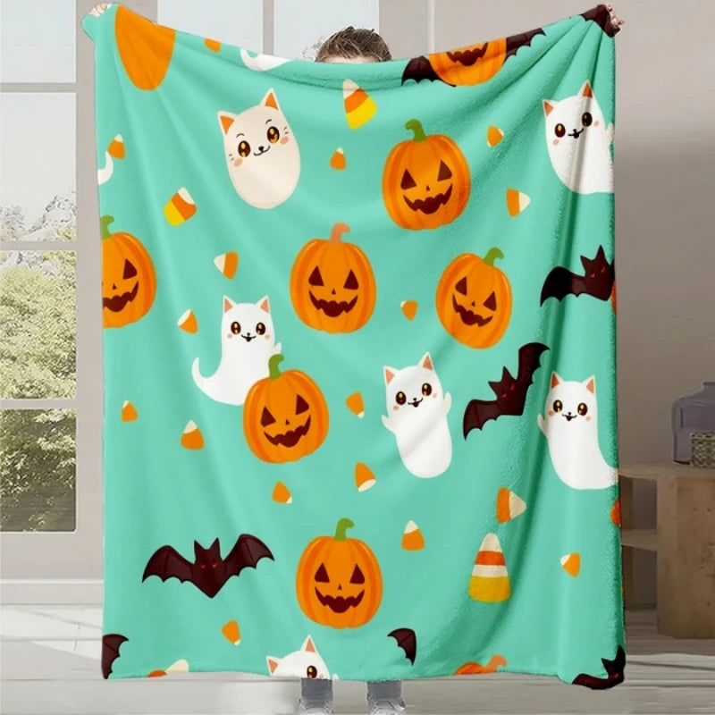 Couverture douce et colorée avec des motifs d'Halloween, chats blancs mignons et citrouilles souriantes sur un fond turquoise.