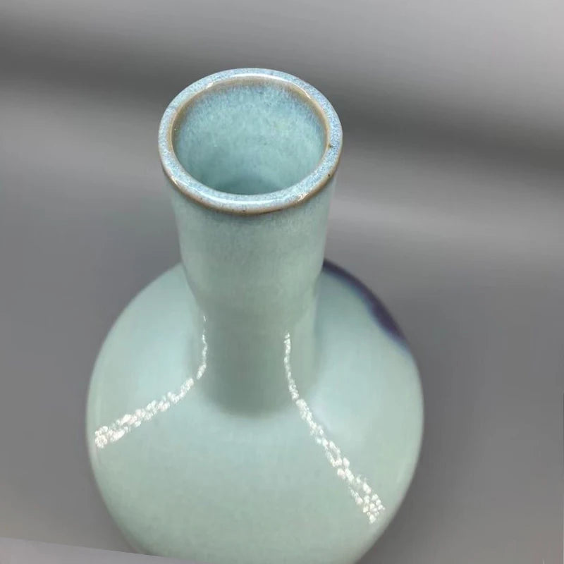 Vase en céramique glazuré vert pastel avec une forme allongée et une base large.