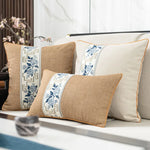 Des coussins décoratifs de couleurs beige et bleu ornés de motifs floraux élégants, disposés sur un canapé dans un décor moderne et raffiné.