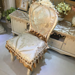 Chaise de style vintage richement ornée de motifs floraux dorés et d'une dentelle délicate, placée près d'un meuble décoratif sur un sol carrelé.