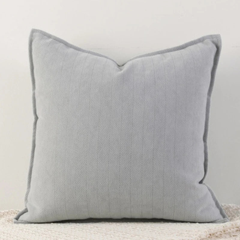 Coussin gris décoratif avec un motif en chevrons sur une surface beige texturée.