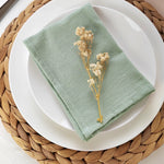Linge de table vert olive avec un joli bouquet de fleurs séchées sur une assiette blanche posée sur un dessous de plat en paille.