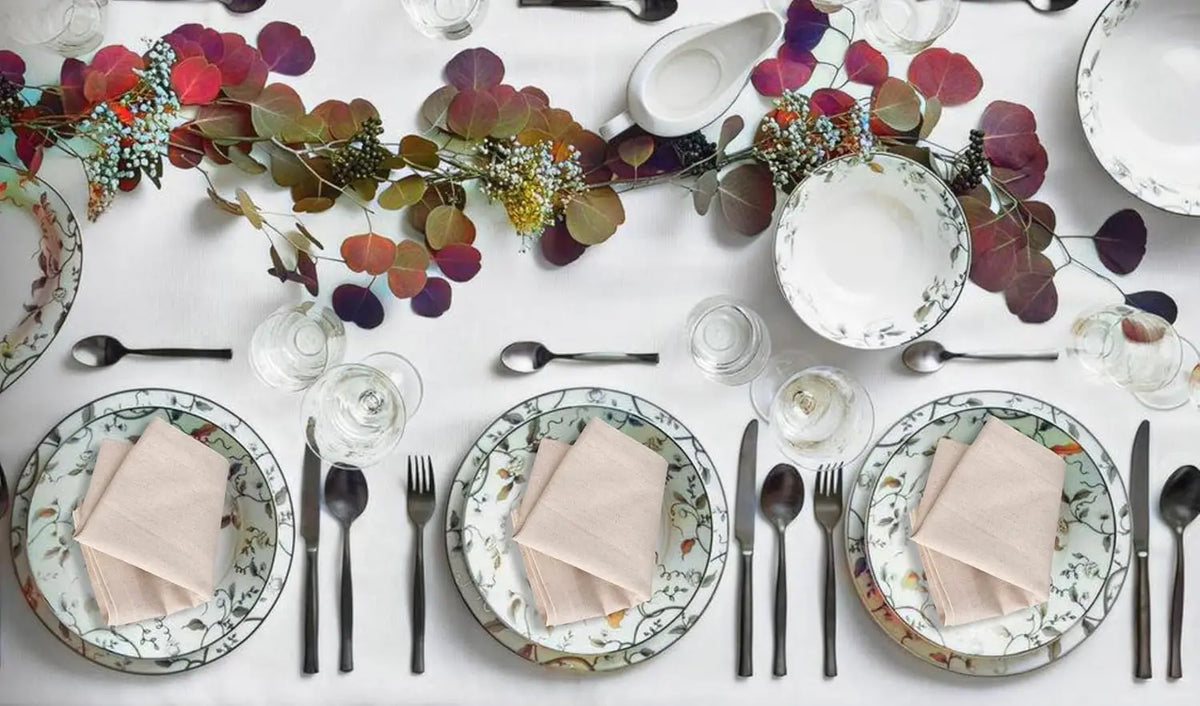 Une élégante table de fête dressée avec de la vaisselle décorée de motifs floraux et accompagnée de belles touches de verdure et de fleurs.