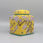 Ce pot de stockage en céramique jaune est orné de motifs floraux roses et de papillons, créant une impression de nature printanière.