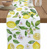 Une nappe blanche ornée de citrons jaunes, de feuillage vert et de délicates fleurs violettes, évoquant une ambiance fraîche et printanière.