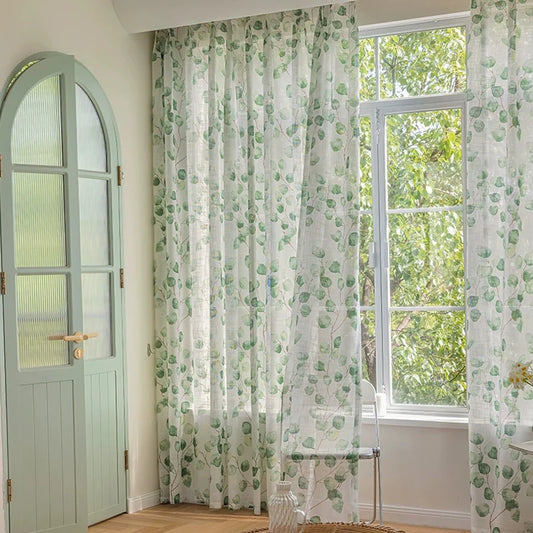 Rideaux voilages à motifs feuillage vert couvrant une baie vitrée à côté d'une porte arquée vert pâle.