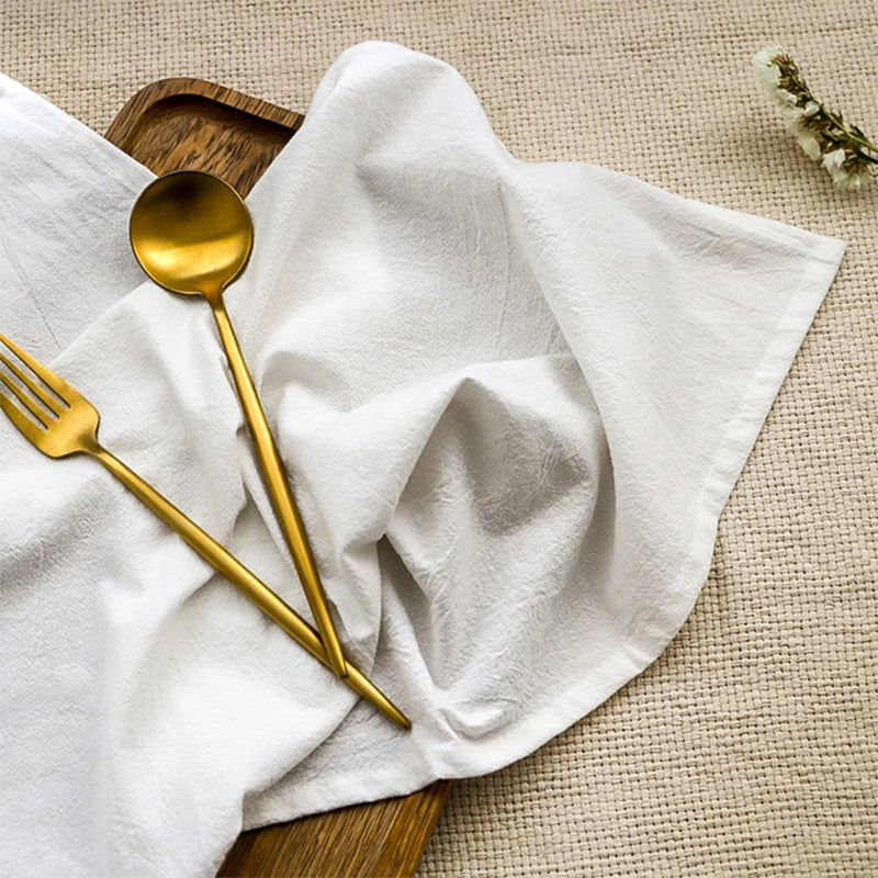 Ensemble d'ustensiles de table en or sur une serviette blanche, sur un fond texturé beige.