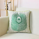 L'image montre un coussin décoratif blanc et vert avec un motif de plume de paon brodé, offrant une touche de fraîcheur et d'élégance à l'environnement.
