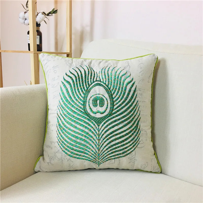 L'image montre un coussin décoratif blanc et vert avec un motif de plume de paon brodé, offrant une touche de fraîcheur et d'élégance à l'environnement.