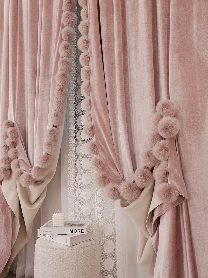 Paire de rideaux rose poudré en velours avec pompons décoratifs et voilage blanc en dentelle, créant une ambiance douce et élégante.