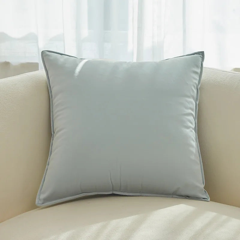 Coussin décoratif gris clair posé sur un canapé crème, dans un intérieur lumineux et apaisant.