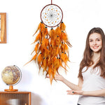 Une jeune femme souriante tient une grande attrape-rêves orange décoré de plumes vibrantes et d'éléments décoratifs.