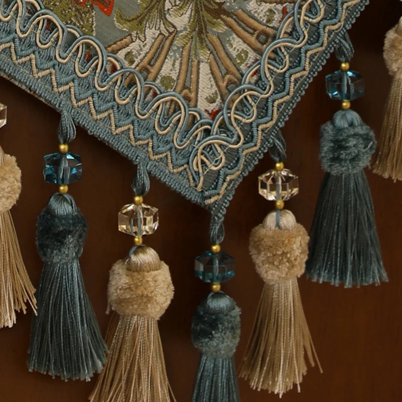 Cette image montre un ornement décoratif avec des franges, des pompons et des perles en couleurs sombres qui créent un motif ornemental élégant et raffiné.