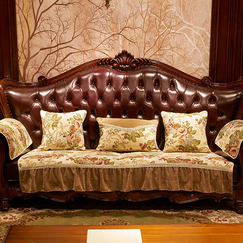 Un canapé vintage en cuir marron foncé avec un dossier capitonné, orné de coussins aux motifs floraux et de détails sculptés sur le haut du dossier.