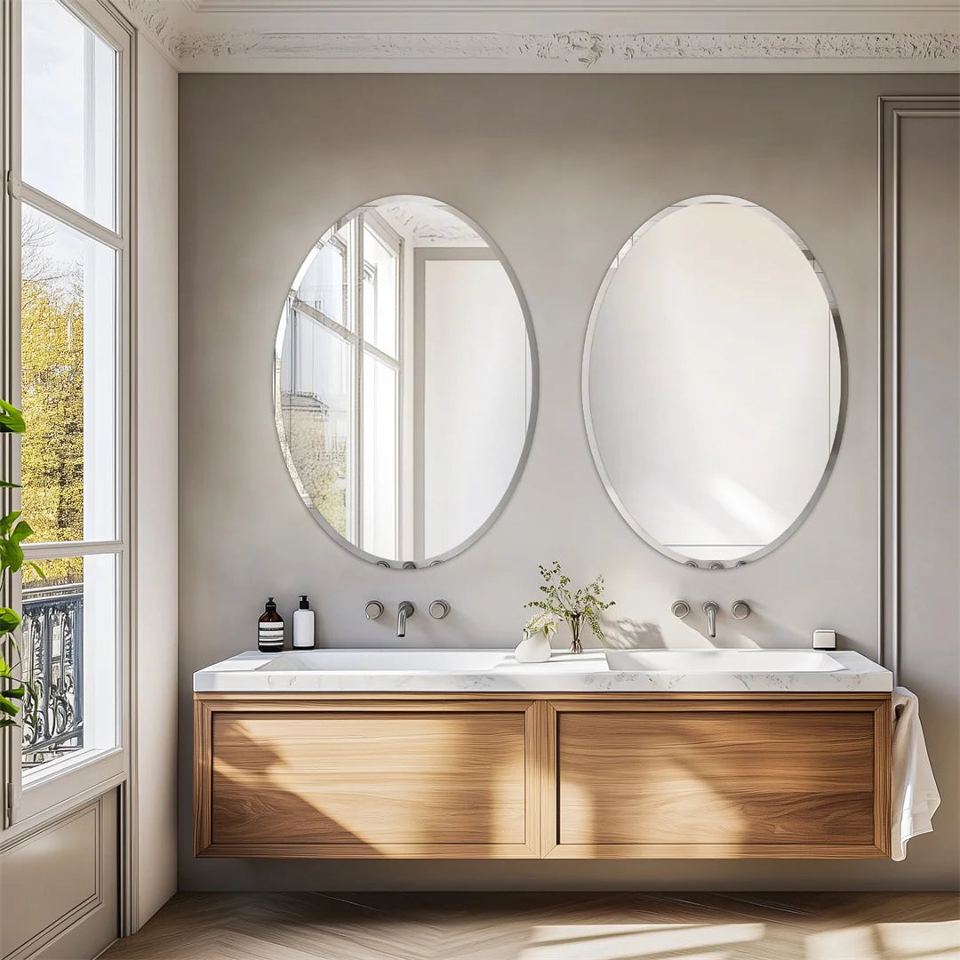 Salle de bain moderne avec deux grands miroirs ovales, un meuble-lavabo en bois et une fenêtre laissant entrer la lumière naturelle.