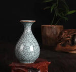 Un vase en céramique blanche ornée de motifs craquelés, entouré de feuilles vertes et de fleurs rouges sur un fond sombre.
