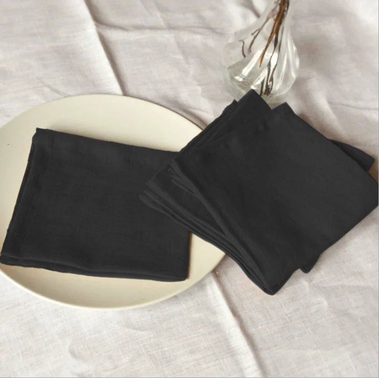 Des serviettes noires pliées sont placées sur une assiette blanche avec un vase en verre, créant une image élégante et épurée.