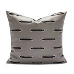 Coussin décoratif gris clair avec motifs brodés de cordons noirs.