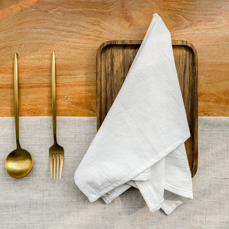 Une assiette en bois avec une serviette blanche, une cuillère et une fourchette dorées, sur un fond de bois clair.