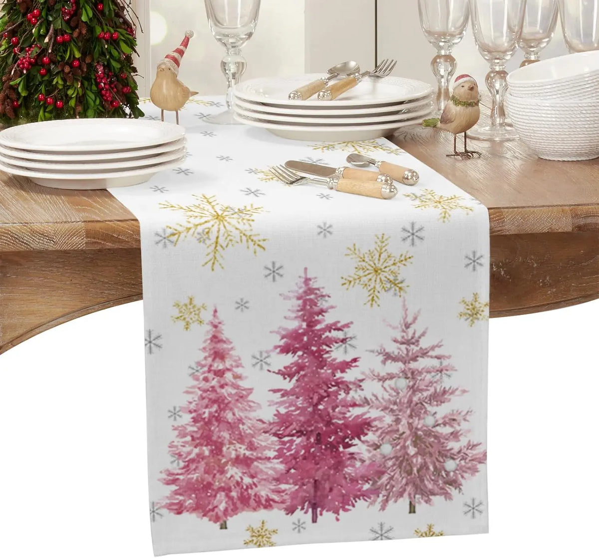 Une table dressée avec des assiettes blanches, des couverts dorés et un chemin de table orné de motifs d'arbres de Noël roses et de flocons de neige.