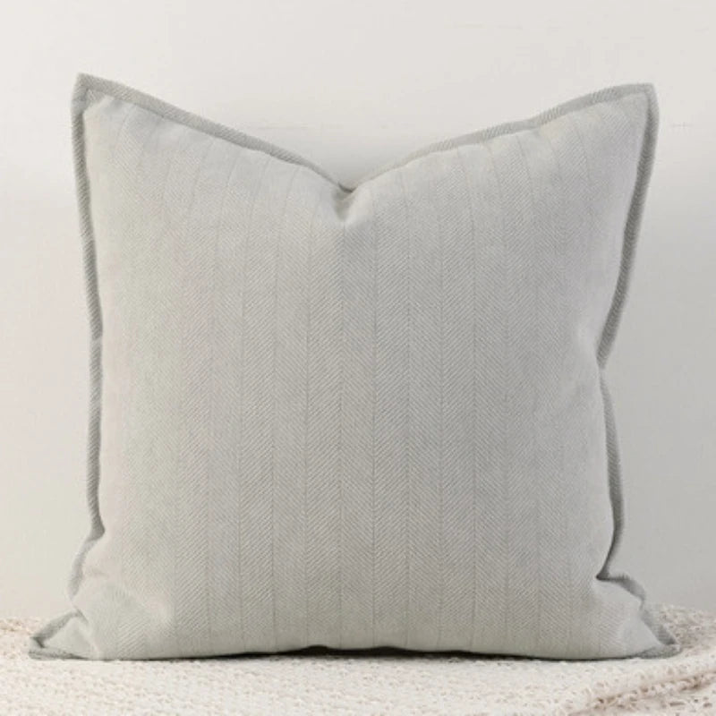 Coussin décoratif gris avec un motif de chevrons sur une surface blanche lisse.