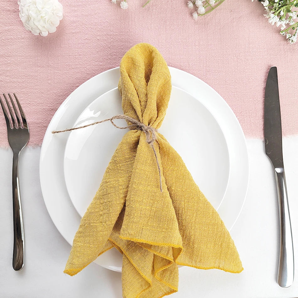 Une assiette blanche avec une serviette jaune pliée en forme de nœud sur un fond rose, accompagnée d'une fourchette et d'un couteau.