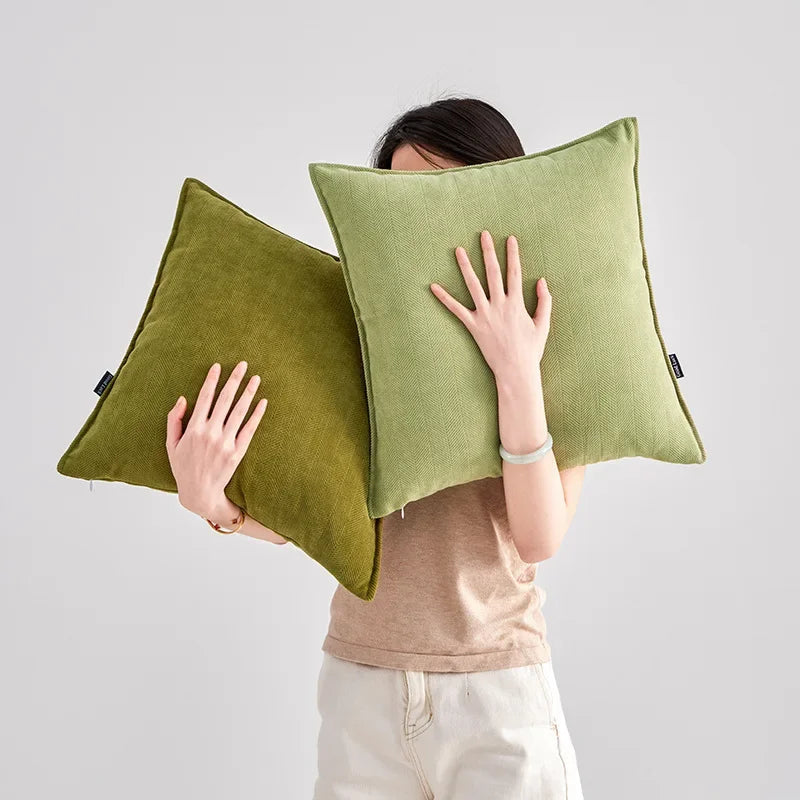 Deux coussins verts translucides cachent partiellement le visage d'une femme, ne laissant visible que ses mains qui les tiennent. Cette image capture un moment intime où la femme semble se cacher ou se dissimuler derrière ces coussins.