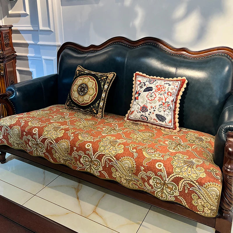 Un élégant canapé en cuir vert foncé orné de coussins décorés de motifs floraux colorés et de bordures de dentelle complexes, posé sur un sol en marbre.