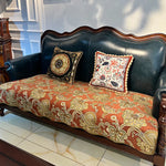 Un élégant canapé en cuir vert foncé orné de coussins décorés de motifs floraux colorés et de bordures de dentelle complexes, posé sur un sol en marbre.