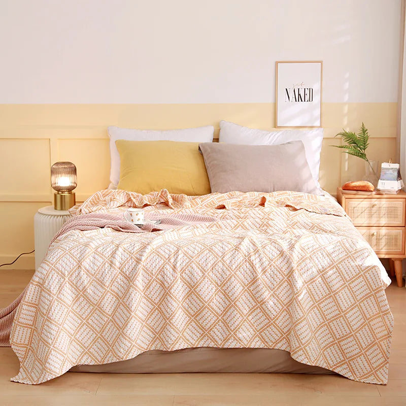 Une chambre design avec un lit moelleux, des coussins gris et une couverture motifs géométriques aux couleurs douces.