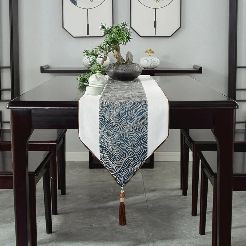 Une table élégante avec des chaises en bois foncé, un chemin de table à motifs bleu et blanc, ainsi que des décorations végétales et ornementales.