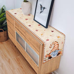 Un meuble en bois décoré d'une nappe aux motifs d'automne, avec une vase et un cadre mural, dans un décor de style scandinave.