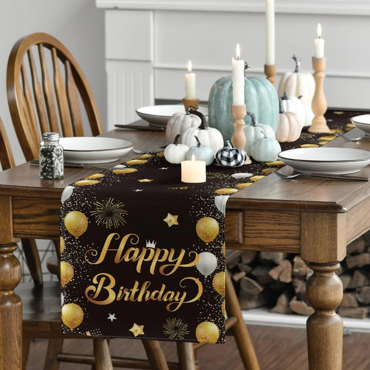Une table de salle à manger décorée d'une nappe noire avec des motifs dorés de ballons et d'étoiles, ainsi que de bougies blanches et de citrouilles peintes de différentes couleurs.