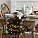 Une table de salle à manger décorée d'une nappe noire avec des motifs dorés de ballons et d'étoiles, ainsi que de bougies blanches et de citrouilles peintes de différentes couleurs.